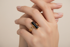 Gold ring with a black stone on a hand against a neutral background