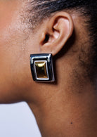 Close-up of an ear wearing a gold and black rectangular earring against a neutral background