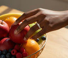 Hand wearing a ring picking up fruit from a fruit basket against a blurry background 