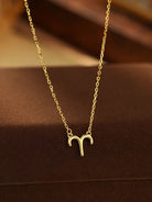 Gold Aries zodiac symbol necklace on a brown background