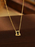 Gold necklace with a Libra zodiac symbol pendant on a brown surface