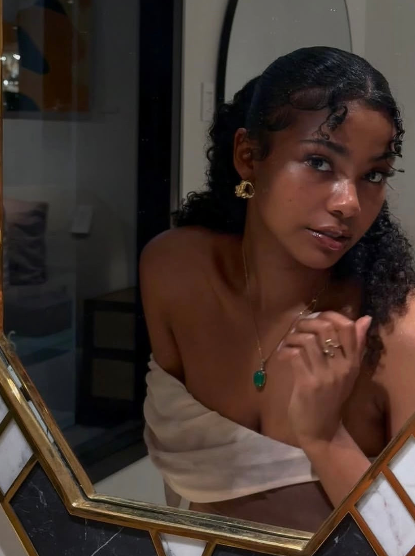 Woman with a gold earring and green necklace in front of a mirror