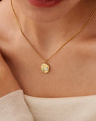 Gold necklace with a pendant on a person wearing a beige top.