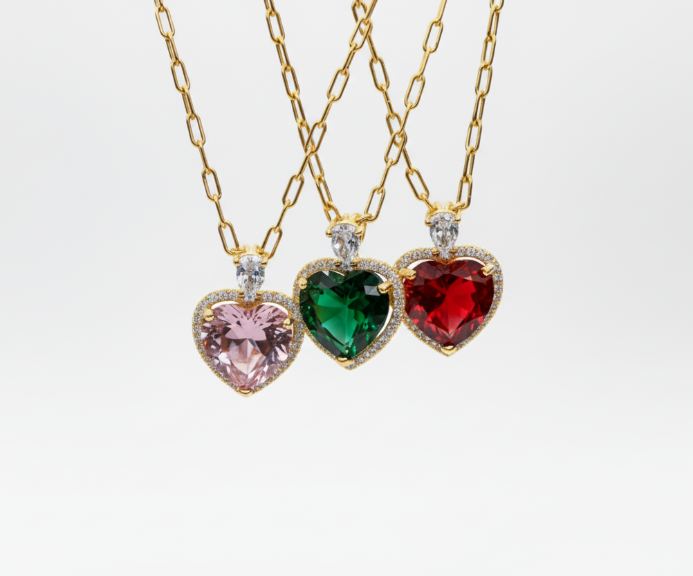 Three heart-shaped gemstone necklaces on gold chains with a blurred background.
