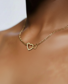 Gold necklace with a heart-shaped clasp on a person's neck against a neutral background