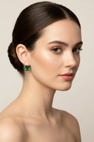 Woman wearing emerald green earrings against a neutral background