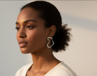 Black woman with a neutral expression wearing a silver geometric earring on a gray background