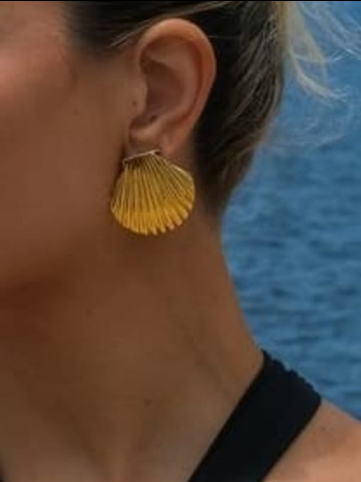 Close-up of a person wearing yellow shell-shaped earrings with a blue background.