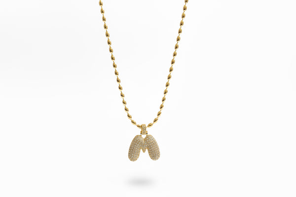 Gold chain necklace with a bubble letter pendant against a white background.
