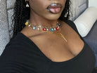 Person wearing a gold necklace with colorful charms in a car.