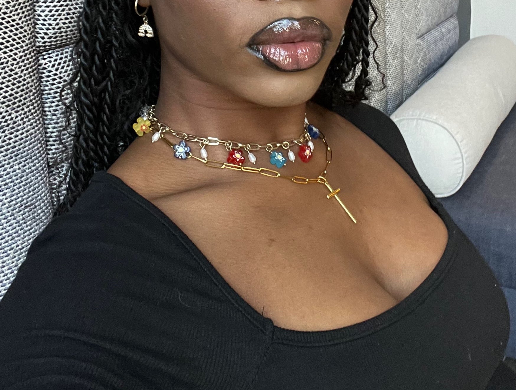Person wearing a gold necklace with colorful charms in a car.