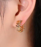 Gold leaf-shaped earring worn on an ear with a blurred background