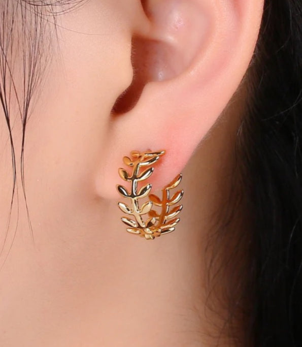 Gold leaf-shaped earring worn on an ear with a blurred background