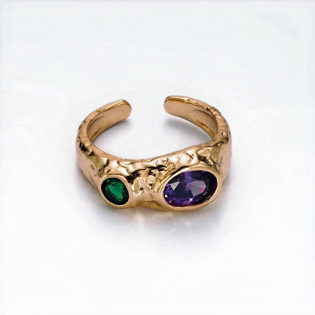 Gold ring with green and purple gemstones on a white background