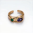 Gold ring with green and purple gemstones on a white background