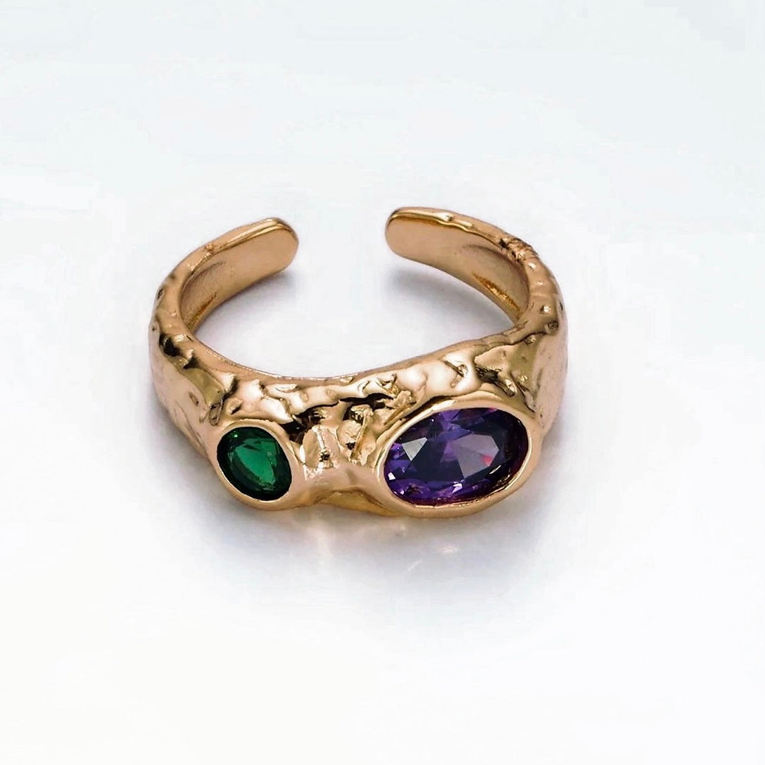 Gold open ring with green and purple gemstones on a white background