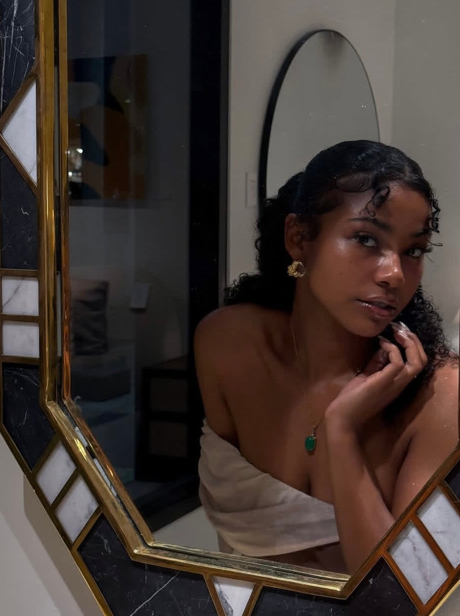 Woman looking at herself in a mirror with a decorative frame earing a green pendant necklace