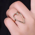 Heart-shaped ring on a hand against a plain background