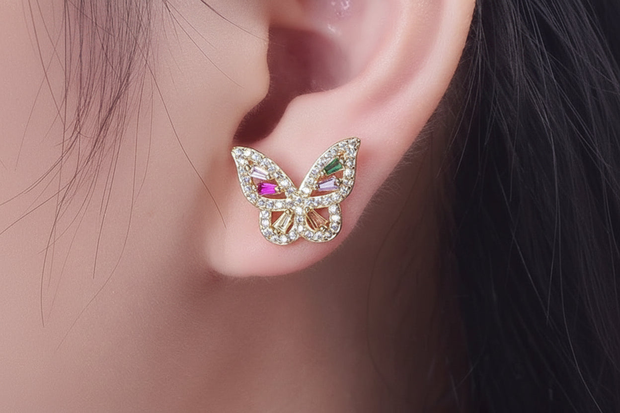Butterfly-shaped earring with colorful gemstones on a person's ear.