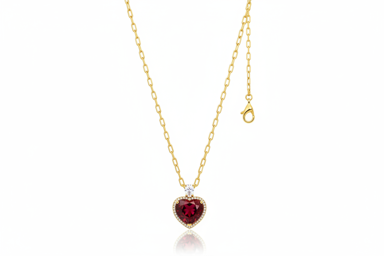 Heart-shaped red gemstone necklace with gold chain on a light pink background