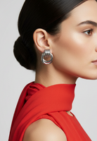 Person wearing a red top on a gray background wearing silver earrings.