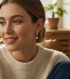 Woman wearing a beige sweater sitting in a cozy living room with plants in the background.
