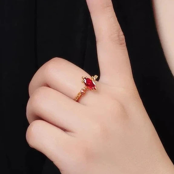 Hand wearing a gold ring with a red gemstone against a black background