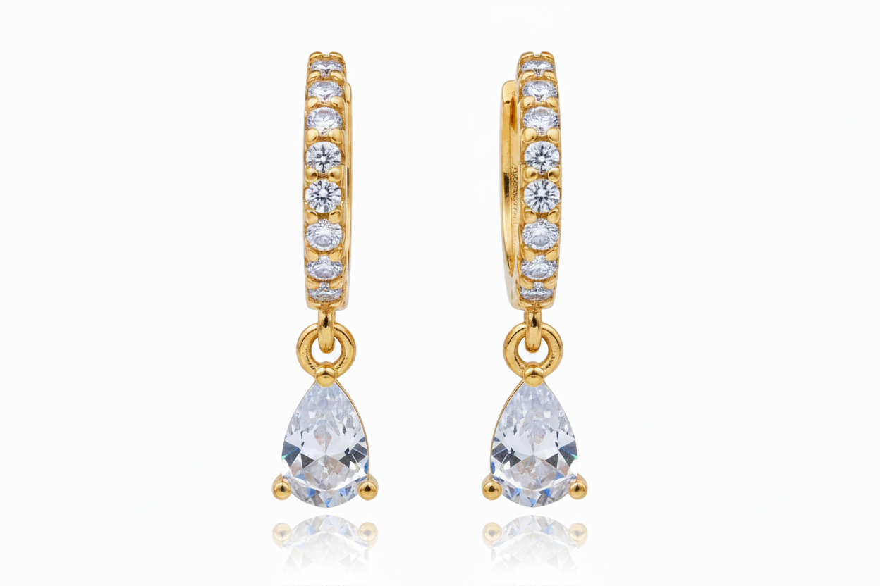 A pair of gold huggie hoop earrings adorned with small clear round-cut stones and featuring a teardrop-shaped clear gemstone dangle, shown against a plain white background.