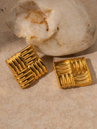 Two gold textured square pendants on a stone surface