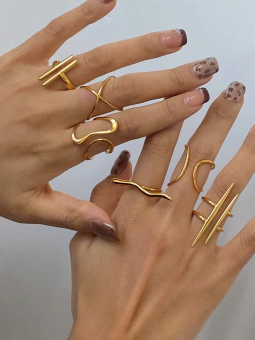 A pair of hands displaying multiple gold-toned wrap rings with various abstract and geometric designs against a plain light gray background.