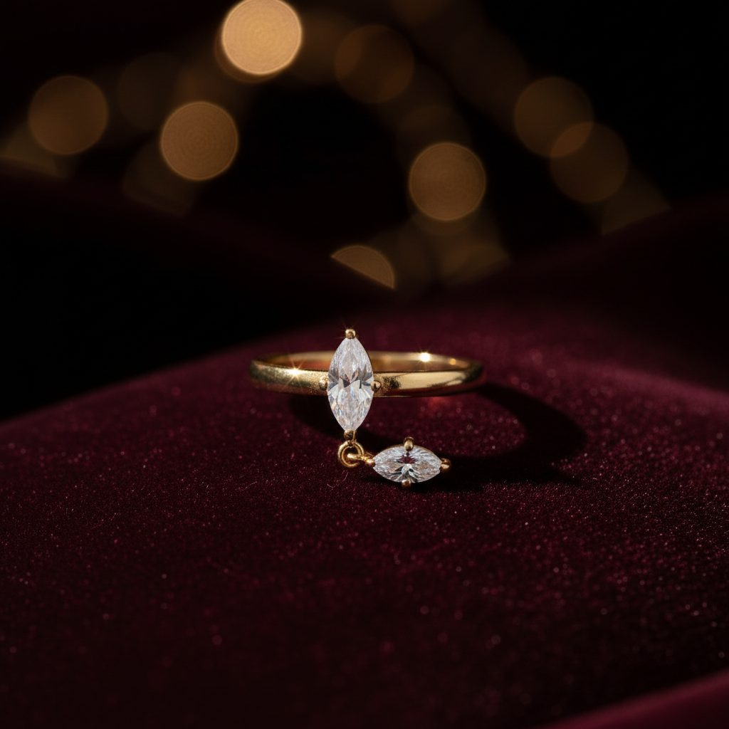 A gold ring featuring a marquise-cut clear gemstone and a smaller marquise-cut clear gemstone dangling below, set against a plain off-white background.