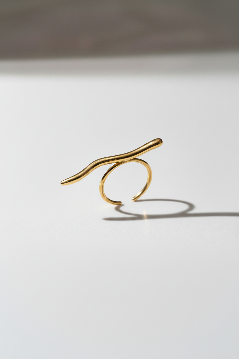 A minimalist silver ring featuring a thin, wavy bar crossing an open circular band, photographed on a clean white surface with a soft shadow.