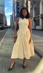 Woman in a light-colored dress standing on a city street with tall buildings.