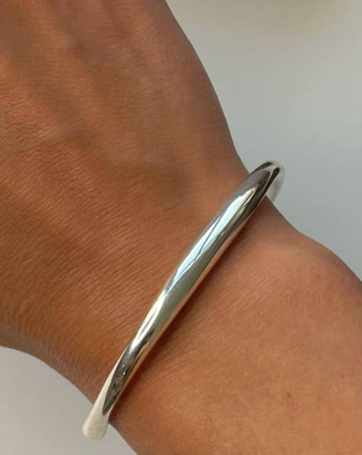 Silver bangle on a wrist with a plain background