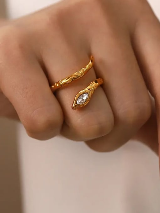 A close-up of a hand wearing two gold rings, one with a textured leaf-like band and the other with a leaf-shaped setting holding a clear marquise gemstone.