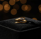A gold snake ring with a clear teardrop crystal, resting on a textured beige stone surface.