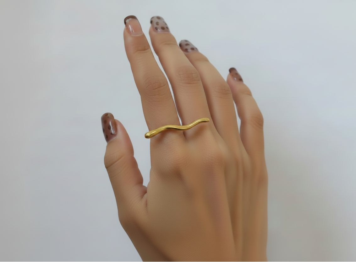 A gold wavy band ring worn on a person's ring finger, shown against a plain light gray background.