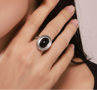 A close-up of a hand wearing a silver ring with a large oval black stone.