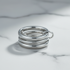 A stack of three polished silver rings with a small attached silver loop, displayed on a white marble surface.
