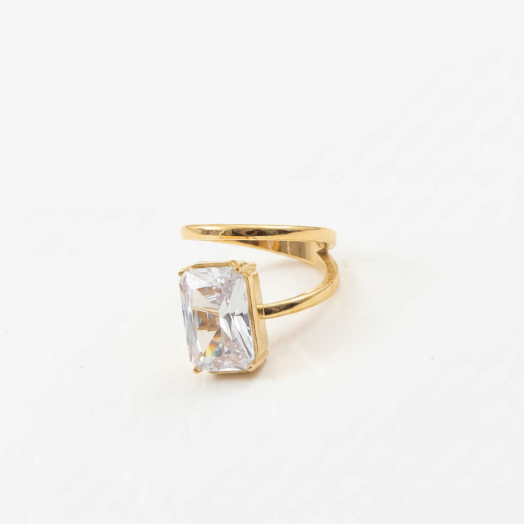 A gold ring featuring a large rectangular clear gemstone in a prong setting, photographed on a plain white background.