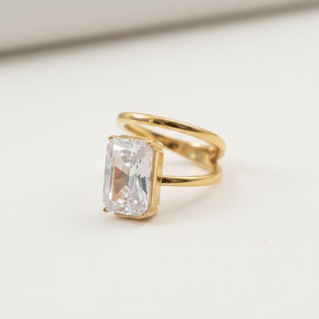 A gold ring with a rectangular clear gemstone in a prong setting, photographed on a clean white background.