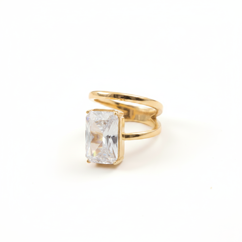 A gold ring featuring a large rectangular clear gemstone in a bezel setting, photographed on a clean white background.