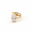 A gold ring featuring a large rectangular clear gemstone in a bezel setting, photographed on a clean white background.