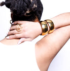 Gold bangles and ring on a person's wrist and hand against a white background
