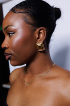 Woman wearing gold earrings and necklace against a white background
