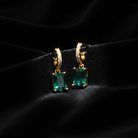 Gold earrings with green gemstones on a dark background