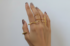 A hand with brown glitter nail polish wearing a stack of gold rings against a plain light gray background.