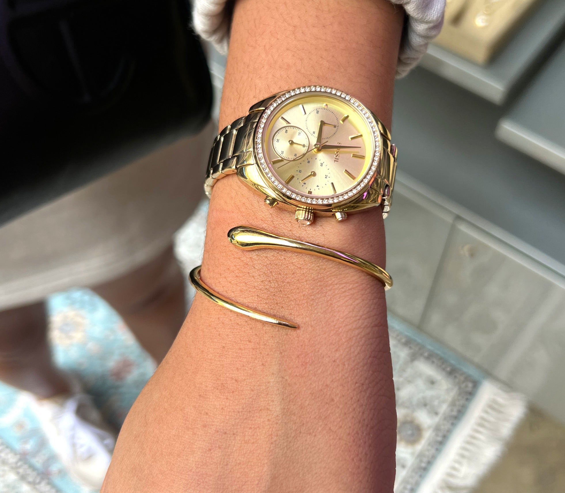 Gold watch and bracelet on a wrist with a blurred background
