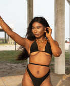 Woman in a black bikini standing outdoors with a neutral background
