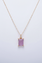 Gold necklace with a purple gemstone pendant on a light gray background